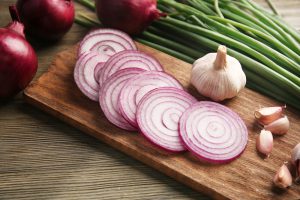 Red onions circles, green onion with garlic on board against wooden background