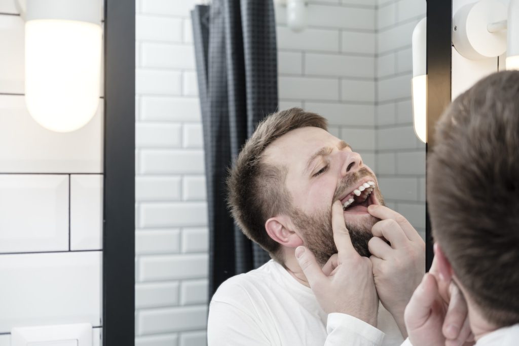 man suffering from tooth decay examines his mouth